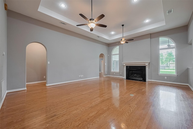 6210 Mahogany Way, Magnolia, TX 77354 - unfurnished living room featuring a tray ceiling, arched walkways, a ceiling fan, light wood-type flooring, and recessed lighting