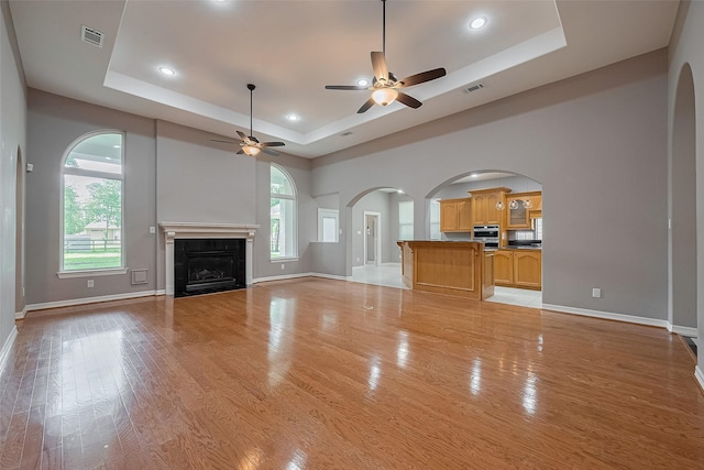 6210 Mahogany Way, Magnolia, TX 77354 - unfurnished living room with a tray ceiling, ceiling fan, arched walkways, light wood-style floors, and recessed lighting