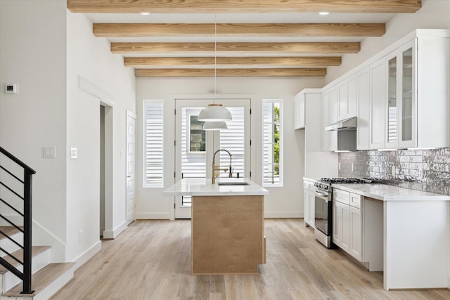 2221 Bevis St, Houston, TX 77008 - kitchen with stainless steel gas range, under cabinet range hood, beamed ceiling, light countertops, and glass insert cabinets
