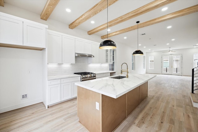 2221 Bevis St, Houston, TX 77008 - kitchen with under cabinet range hood, stainless steel gas range, decorative backsplash, beamed ceiling, and light wood finished floors