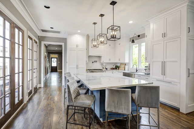 818 Waverly St, Houston, TX 77007 - kitchen featuring white cabinets, dark wood-style flooring, ornamental molding, a kitchen island, and a chandelier