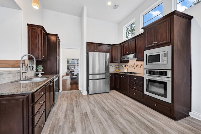135 Wisteria Walk Cir, The Woodlands, TX 77381 - kitchen with stainless steel appliances, dark stone counters, light wood-style floors, decorative backsplash, and a high ceiling