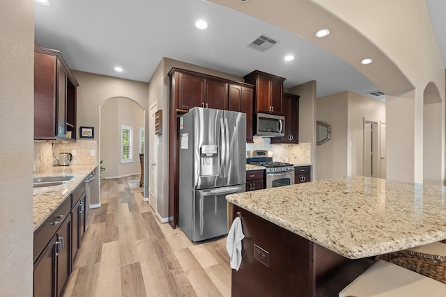6619 Crystal Forest Trl, Katy, TX 77493 - kitchen with stainless steel appliances, arched walkways, light wood-style flooring, decorative backsplash, and light stone countertops