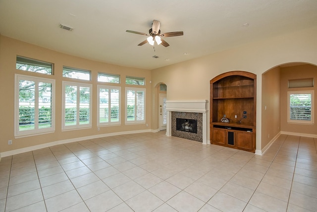 9610 Oakland Lake Way, Missouri City, TX 77459 - unfurnished living room with light tile patterned floors, built in features, ceiling fan, a glass covered fireplace, and arched walkways