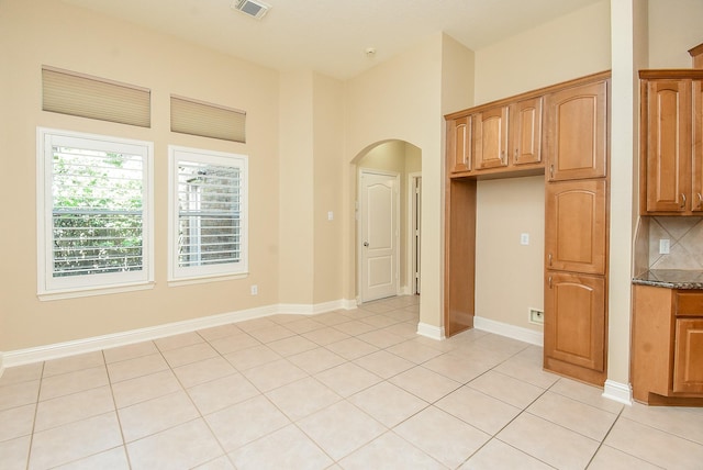 9610 Oakland Lake Way, Missouri City, TX 77459 - kitchen with arched walkways, brown cabinets, decorative backsplash, light tile patterned floors, and dark stone countertops