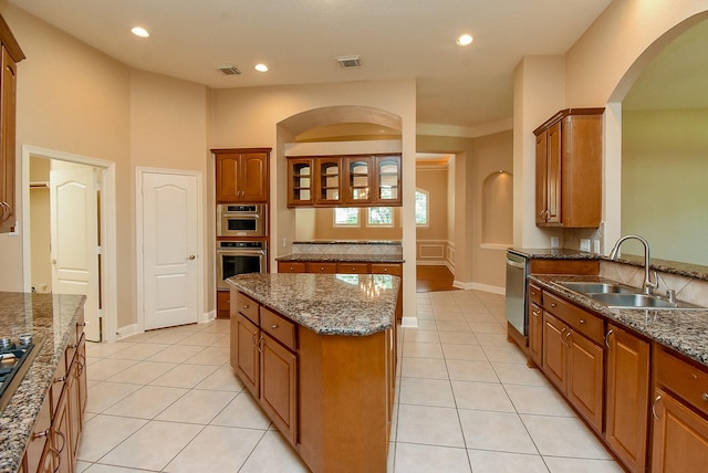 9610 Oakland Lake Way, Missouri City, TX 77459 - kitchen with stainless steel appliances, light tile patterned flooring, arched walkways, brown cabinets, and a kitchen island