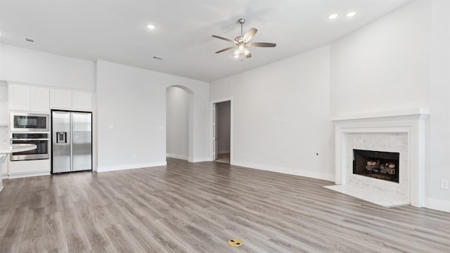 15139 Botanical Garden Dr, Conroe, TX 77302 - unfurnished living room featuring a ceiling fan, arched walkways, light wood finished floors, recessed lighting, and a fireplace with flush hearth