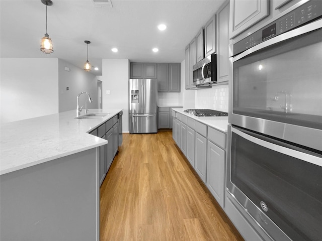 25621 Ramsey Heights Way, Porter, TX 77365 - kitchen with stainless steel appliances, gray cabinetry, light wood-type flooring, decorative backsplash, and decorative light fixtures