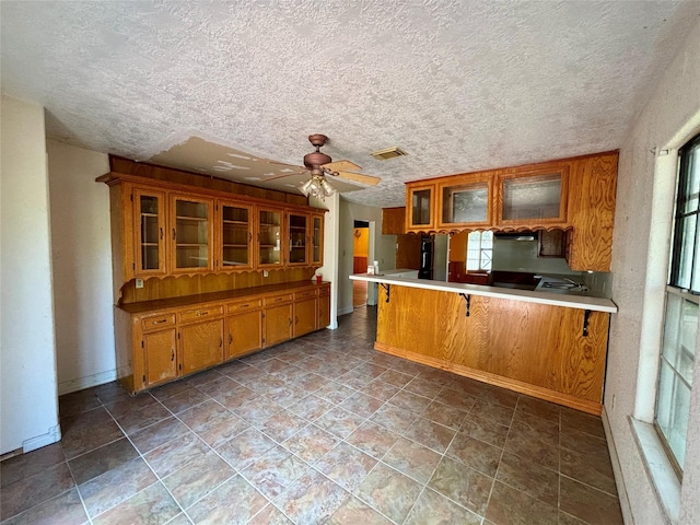 7947 Moore Dr, Pearland, TX 77584 - kitchen featuring brown cabinetry, a textured ceiling, a peninsula, glass insert cabinets, and a breakfast bar