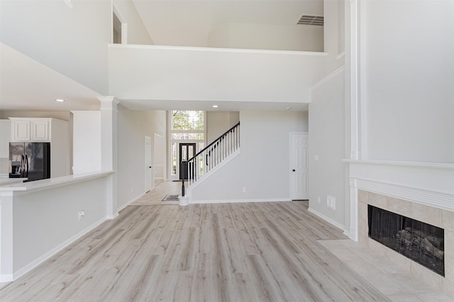 7147 Hot Creek Trce, Humble, TX 77346 - unfurnished living room featuring light wood-style flooring, stairs, a tiled fireplace, a high ceiling, and recessed lighting