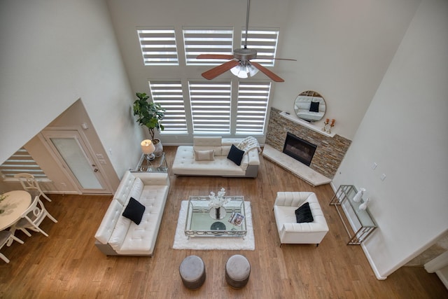 5506 Bellingen River Ln, Sugar Land, TX 77479 - living room featuring a towering ceiling, a ceiling fan, a stone fireplace, wood finished floors, and plenty of natural light