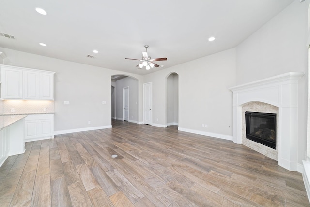 13727 Pedernales Ct, Cypress, TX 77429 - unfurnished living room with light wood finished floors, a glass covered fireplace, ceiling fan, arched walkways, and recessed lighting