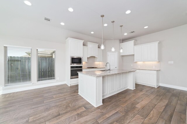 13727 Pedernales Ct, Cypress, TX 77429 - kitchen with stainless steel appliances, tasteful backsplash, light wood-style floors, white cabinets, and light stone countertops