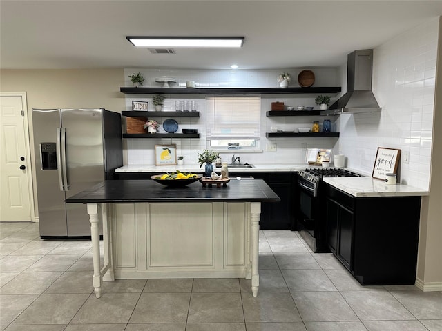 318 N 4th St, Alvin, TX 77511 - kitchen featuring wall chimney range hood, open shelves, stainless steel fridge with ice dispenser, black gas range oven, and dark cabinets
