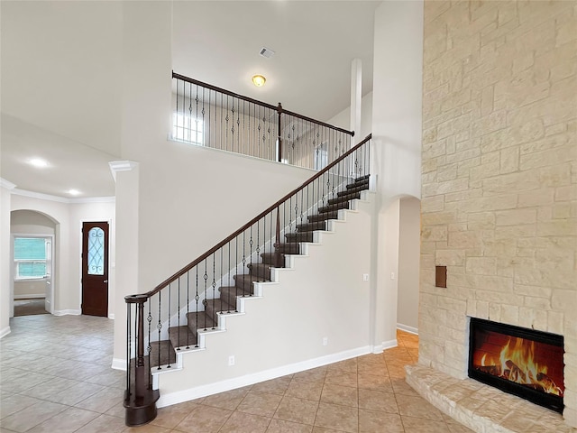 18614 Rimini Ridge Ct, Cypress, TX 77429 - staircase with arched walkways, a high ceiling, tile patterned floors, a stone fireplace, and ornamental molding