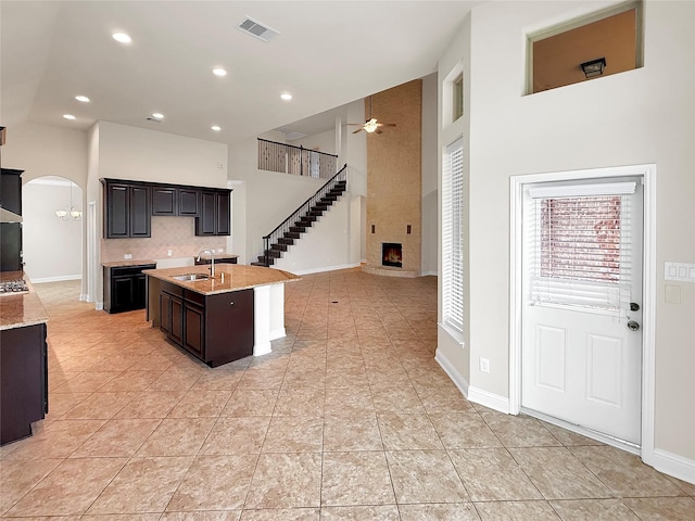 18614 Rimini Ridge Ct, Cypress, TX 77429 - kitchen featuring a fireplace, arched walkways, a ceiling fan, an island with sink, and tasteful backsplash
