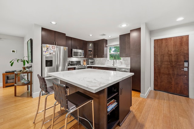 7539 Santa Fe Dr, Houston, TX 77061 - kitchen with appliances with stainless steel finishes, a breakfast bar area, light wood-style flooring, dark brown cabinets, and recessed lighting
