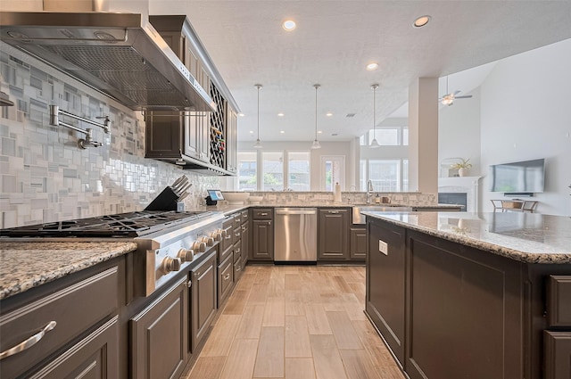 4107 Rainflower Ct, Fulshear, TX 77441 - kitchen with appliances with stainless steel finishes, wall chimney range hood, backsplash, light stone counters, and recessed lighting