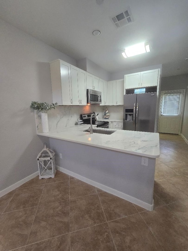 176 Capetown, Conroe, TX 77356 - kitchen featuring appliances with stainless steel finishes, a peninsula, white cabinets, decorative backsplash, and tile patterned floors