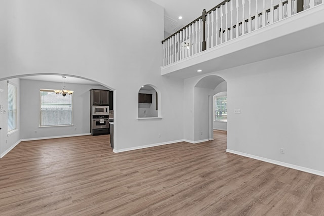 5918 Mahogany Way, Magnolia, TX 77354 - unfurnished living room featuring a high ceiling, a chandelier, light wood-style floors, recessed lighting, and arched walkways
