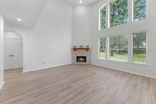 5918 Mahogany Way, Magnolia, TX 77354 - unfurnished living room featuring a towering ceiling, plenty of natural light, light wood-style floors, a warm lit fireplace, and recessed lighting