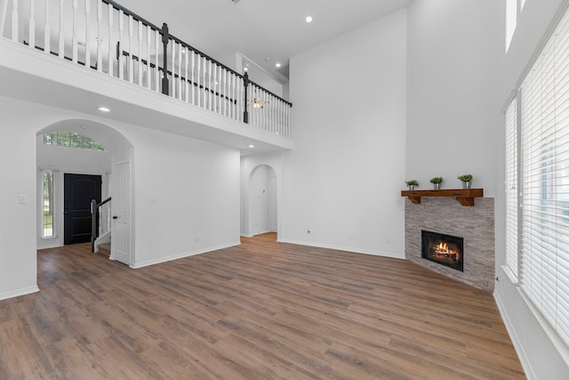 5918 Mahogany Way, Magnolia, TX 77354 - unfurnished living room featuring a towering ceiling, arched walkways, a stone fireplace, wood finished floors, and recessed lighting