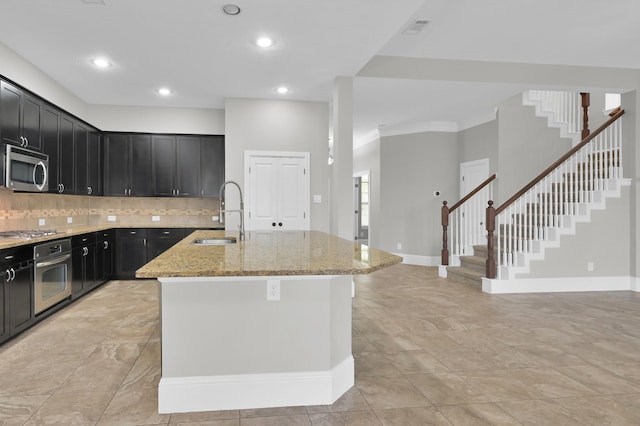 18618 Bridle Grove Ct, Tomball, TX 77377 - kitchen featuring stainless steel appliances, light stone counters, backsplash, a kitchen island with sink, and dark cabinetry