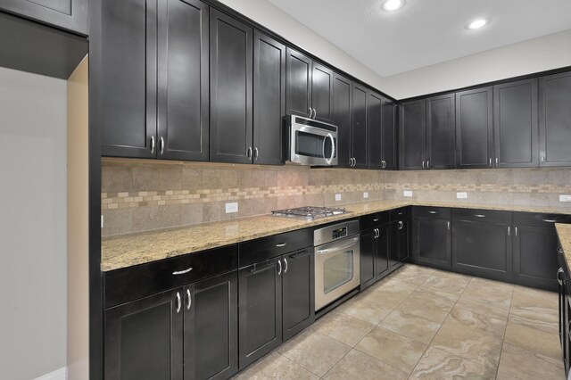 18618 Bridle Grove Ct, Tomball, TX 77377 - kitchen with stainless steel appliances, dark cabinets, decorative backsplash, light stone counters, and recessed lighting