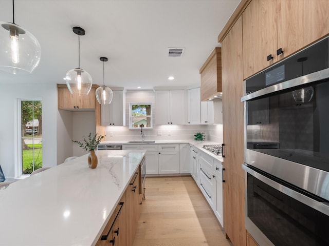 10651 Mayfield Rd, Houston, TX 77043 - kitchen featuring appliances with stainless steel finishes, backsplash, light wood-style flooring, hanging light fixtures, and light stone countertops
