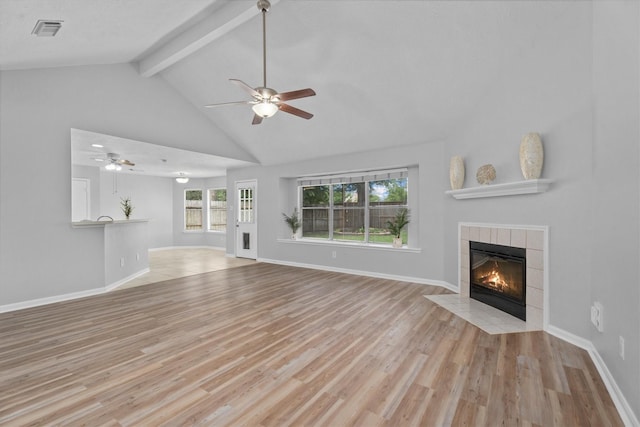 14306 Cypress Meadow Dr, Cypress, TX 77429 - unfurnished living room with a tiled fireplace, ceiling fan, beam ceiling, wood finished floors, and high vaulted ceiling