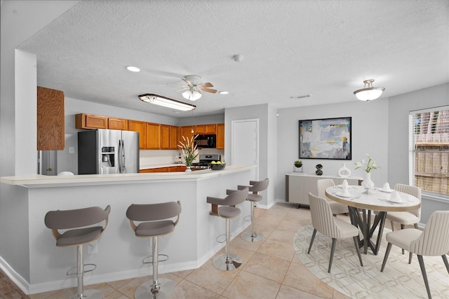 14306 Cypress Meadow Dr, Cypress, TX 77429 - kitchen featuring appliances with stainless steel finishes, light countertops, brown cabinetry, a textured ceiling, and light tile patterned flooring