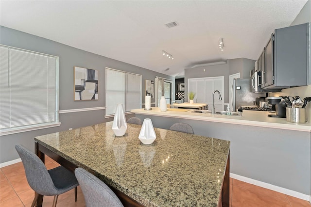 1710 Blue Heather Ln, Fresno, TX 77545 - kitchen with light tile patterned flooring, a peninsula, lofted ceiling, a kitchen bar, and light stone counters