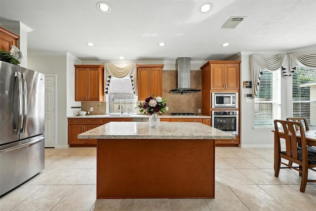 21306 Willowford Park Dr, Katy, TX 77450 - kitchen with appliances with stainless steel finishes, wall chimney exhaust hood, crown molding, a kitchen island, and brown cabinets