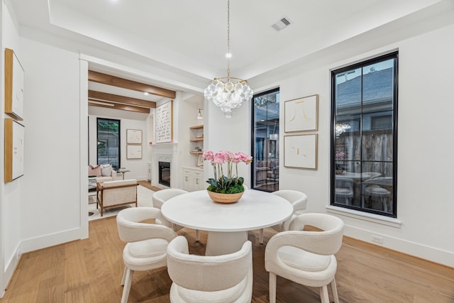 1310 Willard, Houston, TX 77006 - dining area with light wood-type flooring, a chandelier, a glass covered fireplace, and beamed ceiling