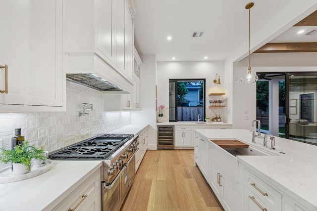 1310 Willard, Houston, TX 77006 - kitchen with beverage cooler, double oven range, light wood-style floors, light stone countertops, and white cabinetry