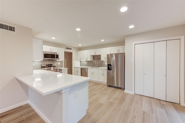 22843 Post Gate Dr, Spring, TX 77373 - kitchen featuring appliances with stainless steel finishes, decorative backsplash, a peninsula, white cabinets, and light wood finished floors