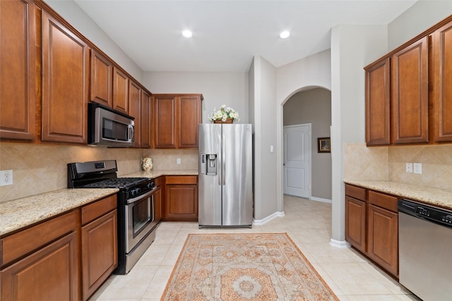 28035 Emma Gardens Ln, Spring, TX 77386 - kitchen featuring appliances with stainless steel finishes, arched walkways, decorative backsplash, light stone counters, and light tile patterned flooring