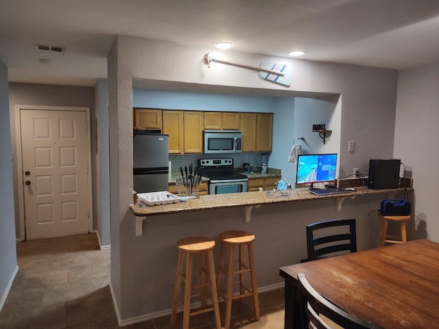 3125 Hells Gate Loop Unit 29, Strawn, TX 76475 - kitchen with appliances with stainless steel finishes, a peninsula, a breakfast bar area, light stone counters, and recessed lighting