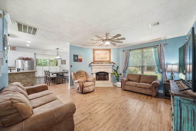 6107 Kyle Bend Ln, Katy, TX 77493 - living area featuring light wood-style flooring, ceiling fan, ornamental molding, a fireplace with raised hearth, and a textured ceiling