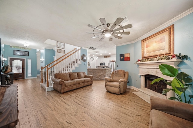 6107 Kyle Bend Ln, Katy, TX 77493 - living room featuring stairs, a fireplace with raised hearth, a ceiling fan, light wood finished floors, and ornamental molding