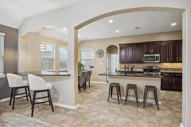 213 Lighthouse Bay Ln, League City, TX 77539 - kitchen with appliances with stainless steel finishes, dark countertops, a kitchen breakfast bar, backsplash, and dark brown cabinetry