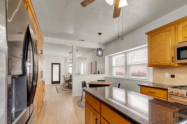 10603 Wagon Trail Rd, Houston, TX 77064 - kitchen featuring freestanding refrigerator, stainless steel microwave, decorative backsplash, light wood-style flooring, and dark stone countertops