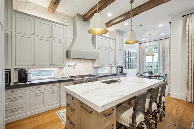 3835 Merrick St, Houston, TX 77025 - kitchen featuring premium range hood, light wood finished floors, an island with sink, decorative backsplash, and beam ceiling