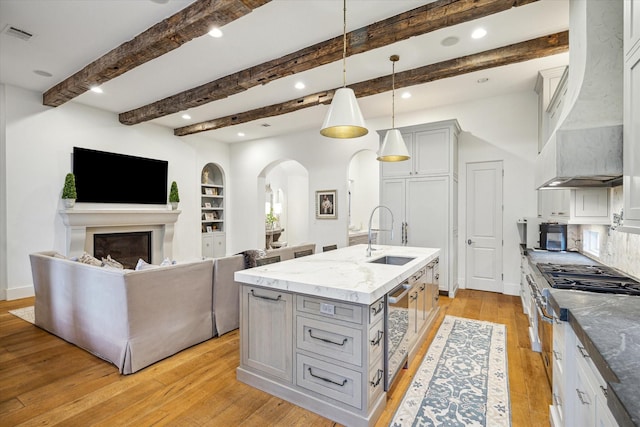 3835 Merrick St, Houston, TX 77025 - kitchen with wall chimney exhaust hood, arched walkways, stainless steel appliances, a center island with sink, and light wood-style floors