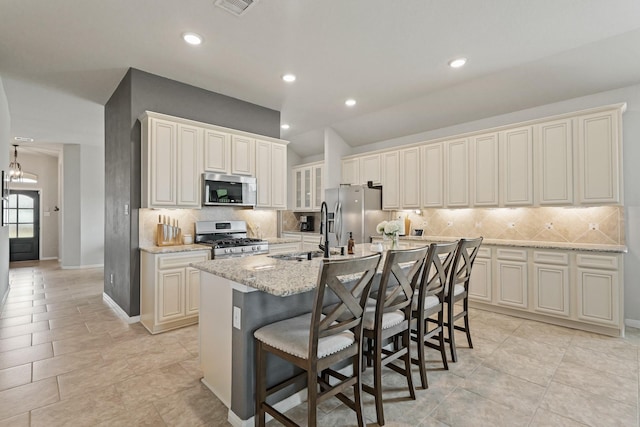 18015 Van Berkel Ln, Houston, TX 77044 - kitchen featuring appliances with stainless steel finishes, a center island with sink, tasteful backsplash, light stone counters, and a kitchen bar