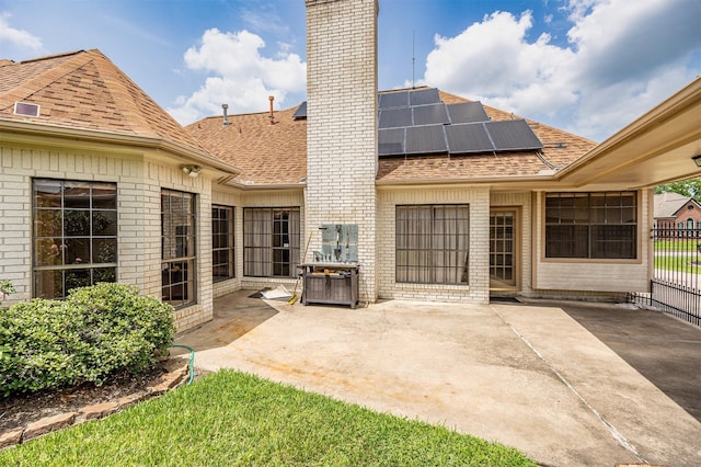 4417 Alamance St, Baytown, TX 77521 - back of house featuring roof with shingles, brick siding, roof mounted solar panels, a chimney, and a patio area