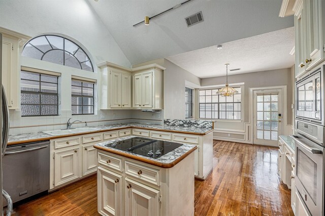 4417 Alamance St, Baytown, TX 77521 - kitchen featuring stainless steel appliances, cream cabinetry, a peninsula, wood finished floors, and a textured ceiling