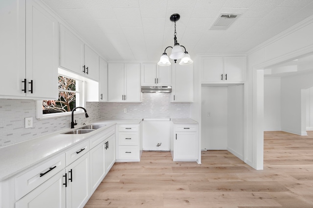 7711 Greenstone St, Houston, TX 77087 - kitchen featuring under cabinet range hood, decorative backsplash, light wood-style flooring, white cabinetry, and pendant lighting