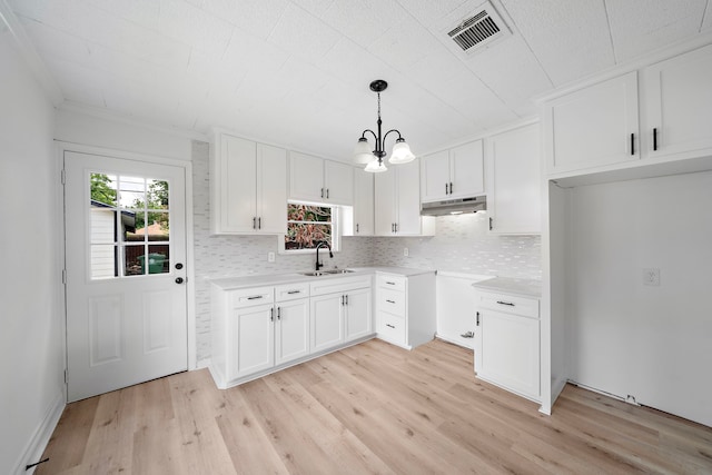 7711 Greenstone St, Houston, TX 77087 - kitchen featuring under cabinet range hood, light wood finished floors, a chandelier, tasteful backsplash, and white cabinets