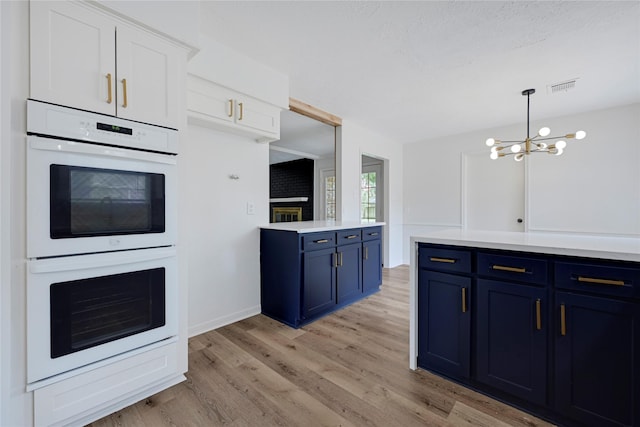 910 Woodchurch Ln, Houston, TX 77073 - kitchen featuring blue cabinetry, white double oven, light wood-style flooring, a chandelier, and light countertops